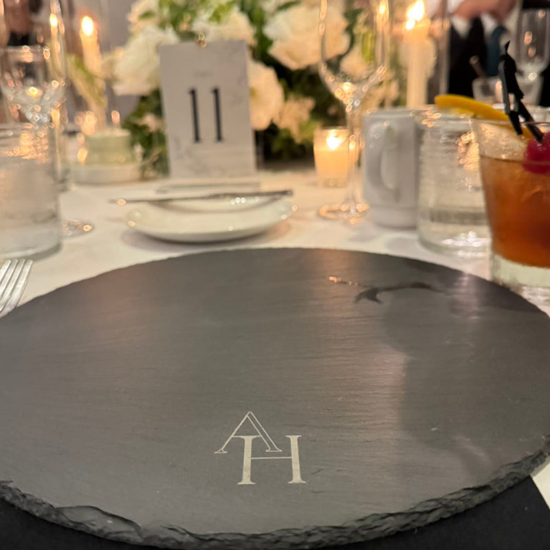 A slate charger engraved with a monogram at a candlelit event table.