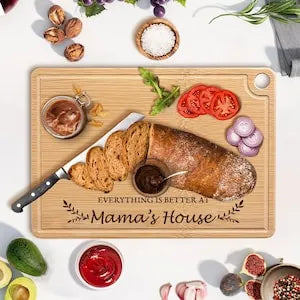 Wooden cutting board with bread and utensils, surrounded by food items on a white surface.