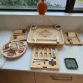 Three-drawer bamboo charcuterie board opened to show side serving trays and center utensil drawer