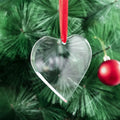 Clear heart-shaped ornament hanging on a red ribbon against a green pine branch background