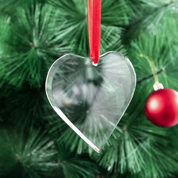Clear heart-shaped ornament hanging on a red ribbon against a green pine branch background