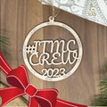 Decorative ornament with '#ITMC CREW 2023' text on a wooden background with a red bow.
