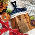 Wooden cutting board with engraved names and date, surrounded by decorative items on a textured surface.