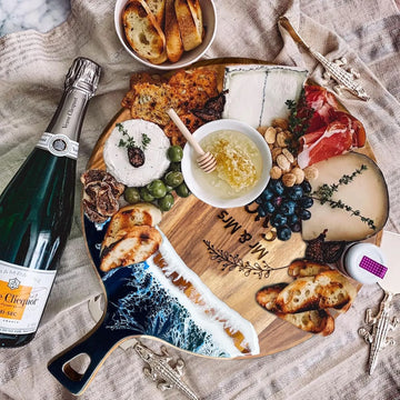 Wooden charcuterie board with assorted cheeses, meats, and bread accompanied by a bottle of champagne.