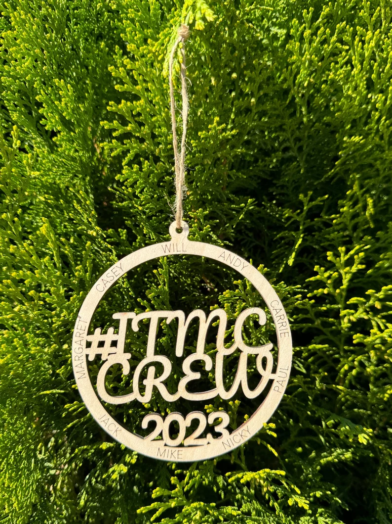 Decorative ornament with '#ITMC CREW 2023' text on a wooden background with a red bow.