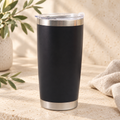 Black 20oz insulated coffee tumbler on warm cream stone