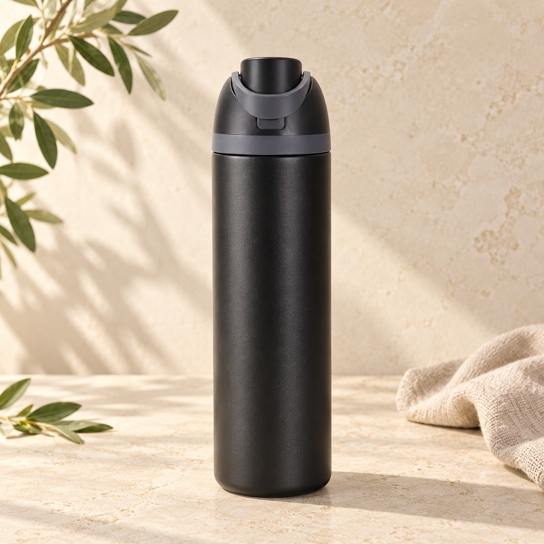Black 24oz sports bottle with straw on warm cream stone